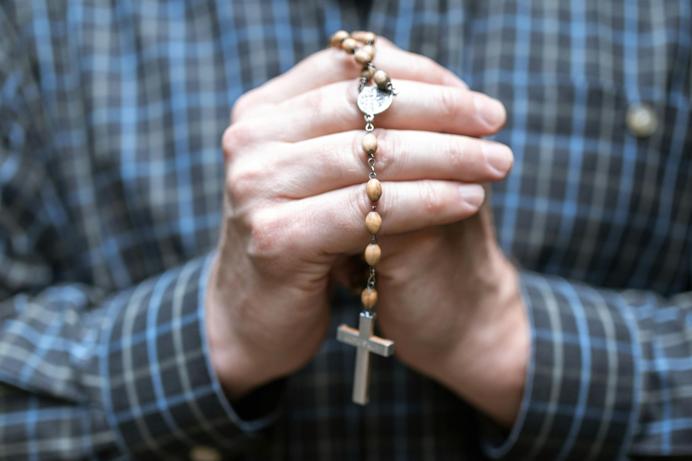 Close-up of a man's hands folded in prayer holding wooden rosary beads